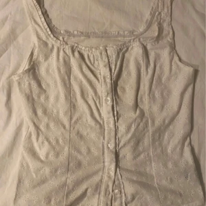 Vit blus från Shein - Säljer en söt vit blus från Shein med knappar framtill. Blusen har ett diskret broderat mönster och elastiska kanter vid hals och ärmar. Perfekt för en somrig look!