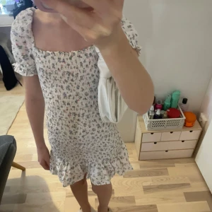 Blommig klänning med puffiga ärmar från Gina Tricot  - Charmig blommig klänning i vitt med små blommor i olika färger. Klänningen har korta puffärmar och en söt volangdetalj vid fållen. Perfekt för en somrig look!