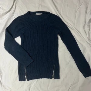 Mörkblå stickad tröja med dragkedjor - Snygg mörkblå stickad tröja med dragkedjor på sidorna. Tröjan har en rund hals och långa ärmar, perfekt för kyligare dagar. En stilren och bekväm tröja som passar till många tillfällen.
