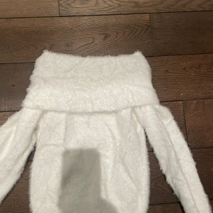 Vit fluffig offshoulder-tröja - Säljer en supermjuk och fluffig vit offshoulder-tröja. Perfekt för att hålla sig varm och stilren under kyliga dagar. Tröjan har långa ärmar och en bred krage som kan bäras ned över axlarna för en trendig look. Skriv vid frågor och bilder, pris kan alltid diskuteras
