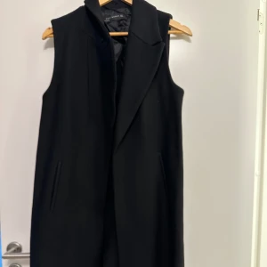 Zara Svart lång väst - Snygg svart lång väst med stilren design. Västen har en klassisk krage och dolda fickor på sidorna. Perfekt för lager-på-lager-stil. Str s använd ett få antal gånger. 
