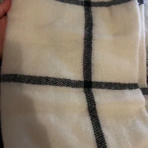 Vit och svart halsduk från H&M - Säljer en stilren vit halsduk med svarta rutor från H&M. Den är supermjuk och perfekt för att hålla dig varm under kyliga dagar. Passar både till vardags och lite finare tillfällen. Mått: 200x65 cm. Perfekt accessoar för att lyfta din outfit! 🖤🤍