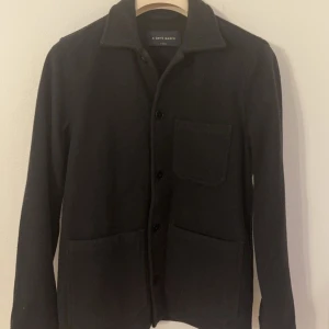 Svart overshirt från A Day's March - Snygg svart overshirt från A Day's March med knappar framtill och praktiska fickor. Den är i bra skick och väldigt fräsch! Den är i 10/10 , anställd ett fåtal gånger.