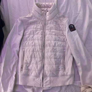 Vit jacka från Parajumpers - Säljer en stilren vit jacka/cardigan från Parajumpers med quiltad design och dragkedja framtill. Jackan har en hög krage och ribbade muddar. Perfekt för kyligare dagar.