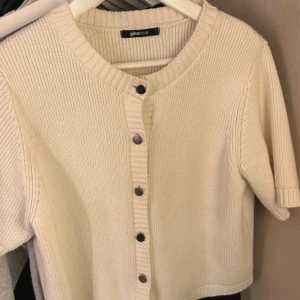 Vit ribbad kofta från Gina Tricot - Säljer en stilren vit kofta från Gina Tricot. Den är ribbad med korta ärmar och har knappar framtill. Perfekt för en avslappnad look.