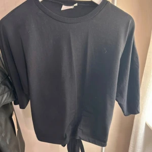 Svart topp från Nelly - Säljer en svart topp från Nelly med knytning vid ryggen. Toppen har trekvartsärmar och en rund halsringning. Perfekt för en stilren look.