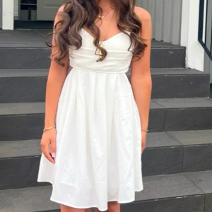 Vit klänning - Säljer en elegant vit klänning med omlott-detalj vid bysten. Klänningen har en vacker, flödande design som passar perfekt för sommarens festligheter. Den är knälång och har en smickrande passform. Användes en gång för student utspring, storlek XS, ser ut som ny! Priset kan diskuteras 