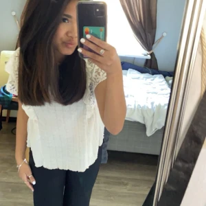 Vit blus med spetsdetaljer - Säljer en söt vit blus med spetsdetaljer på ärmarna och volang längs axlarna. Perfekt för en somrig look. Blusen har en lös passform och är tillverkad i ett lätt material.