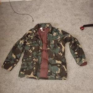 Camouflagejacka från Alaska D&G Products - Säljer en cool camouflagejacka designad av Brian Gregory. Jackan har en quiltad insida och är perfekt för höst och vinter. Den har långa ärmar och praktiska fickor framtill. Varm och skön. Det står ingen strlk, men den passar personer som bär M/medium. Ingen slitage elr liknande, pris kan diskuteras hör gärna av er