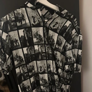 Svartvit kortärmad skjorta med fototryck - Cool svartvit skjorta med unikt fototryck. Perfekt för en avslappnad stil eller en utekväll. Skjortan har korta ärmar och en klassisk krage. Passar bra till jeans eller shorts för en trendig look.