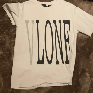Vit och svart t-shirt från VLONE - Två t-shirts från VLONE. Den vita har ett stort svart 'VLONE' tryck på framsidan och ett stort 'V' på baksidan. Den svarta t-shirten har ett porträtttryck på framsidan och ett rött 'V' på baksidan. 300kr st 500kr för båda passar även M