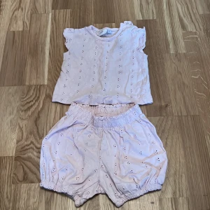Ljusrosa babyset från MyWear - Säljer ett sött ljusrosa babyset från MyWear i storlek 74. Setet består av en ärmlös topp och matchande shorts med elastisk midja. Båda delarna har ett fint broderat mönster. Perfekt för varma sommardagar! 🌸