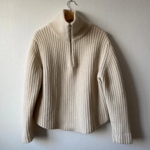 Beige stickad tröja från Eytys - Säljer en stilren beige stickad tröja från Eytys med dragkedja och hög krage. Perfekt för kyliga dagar med sin mysiga och varma design. Tröjan har långa ärmar och en ribbad struktur som ger en klassisk look. Storlek: S Dam & XS Herr - Modell: Neptune - Artnr: J126