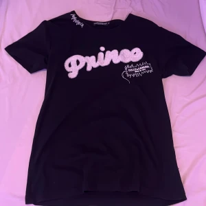 Svart t-shirt från Dolce & Gabbana - Snygg svart t-shirt från Dolce & Gabbana med texten 'Prince' i glittriga bokstäver. T-shirten har korta ärmar och en cool design med broderade detaljer. Perfekt för att ge din outfit en lyxig touch.