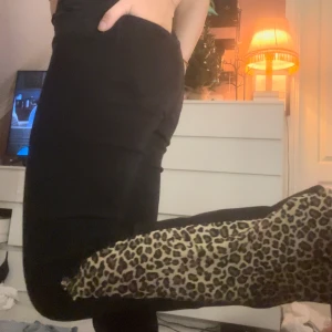 Svarta byxor med leoparddetaljer - Säljer ett par svarta byxor med leopardmönstrade detaljer längs benen. De är tighta och har en snygg passform som framhäver figuren. Perfekta för en utekväll eller när du vill känna dig extra stylish. 🐆✨
