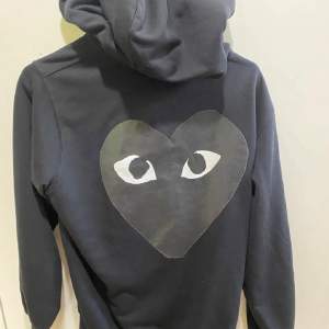 Säljer en svart hoodie från Comme des Garçons med det ikoniska hjärtat med ögon på bröstet och ryggen. Den har dragkedja och justerbara snören i huvan. Perfekt för en stilren och bekväm look. Passar både till vardags och chillkvällar. 🖤