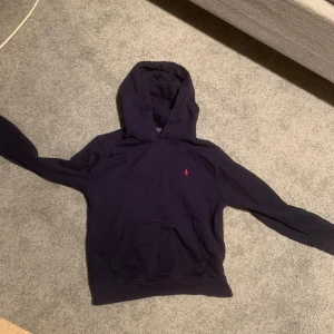Ralph lauren hoodie - Säljer en snygg mörkblå hoodie från Ralph Lauren med den klassiska röda loggan på bröstet. Perfekt för kyliga dagar med sin mjuka och bekväma passform. Den har en stor ficka fram och en skön huva. Passar både till vardags och chillkvällar. 🧢