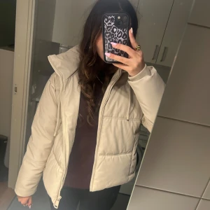 Beige pufferjacka - Säljer en snygg beige pufferjacka i mycket bra skick. Den har en dragkedja framtill och är perfekt för höst och vinter. Jackan är långärmad och har en skön, varm känsla. Perfekt för att hålla sig varm och stilren under kyliga dagar!