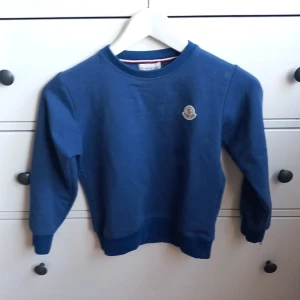 Blå tröja från Moncler - Säljer en snygg blå tröja från Moncler i mycket bra skick. Den har en klassisk rund hals och Monclers ikoniska logga på bröstet. Perfekt för både vardag och lite finare tillfällen. Passar bra till jeans eller chinos för en stilren look.