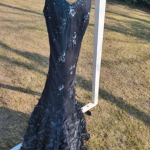 Svart långklänning med paljetter - Elegant svart långklänning med glittriga paljettdetaljer och blommönster. Klänningen har en v-ringad fram och en öppen rygg. Köpte den secondhand som balklänning men den var tyvärr lite för kort för mig som 1,77 så kom aldrig till användning💕