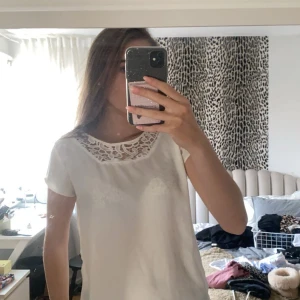Vit blus med spetsdetaljer - Säljer en superfin vit blus med spetsdetaljer vid halsringningen. Perfekt för både vardag och fest! Den har korta ärmar och en lös passform som gör den bekväm att bära hela dagen. Passar perfekt till jeans eller kjol för en chic look. Går att använda åt båda hållen. 