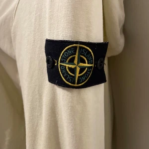 Gul/Beige zipupp hoodie från Stone Island knappt använd kvitto finns också  - Säljer en snygg beige huvtröja från Stone Island. Den har en dragkedja framtill och långa ärmar. Tröjan är i bra skick och har den klassiska Stone Island-loggan på ärmen. Perfekt för höst och vår! Knappt använd och finns även kvitto. Med vänliga hälsningar din plug 