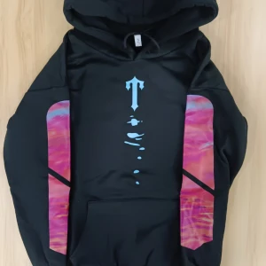 Svart hoodie från Trapstar - Säljer en svart hoodie från Trapstar med coola rosa och lila detaljer på ärmarna och ryggen. Den har en stor luva och en unik design med ett tryck på framsidan. Perfekt för att sticka ut i mängden! 🖤💜