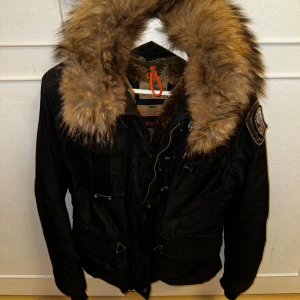Vinterjacka med päls från Parajumpers - Säljer en svart Parajumpers jacka i mycket bra skick. Den har en stor, mysig pälskrage och är fodrad med päls för extra värme. Perfekt för kalla vinterdagar. Jackan har flera praktiska fickor och en dragkedja framtill. En riktig klassiker för vintern! Tveka inte att höra av dig vid eventuella frågor eller bilder❄️☺️