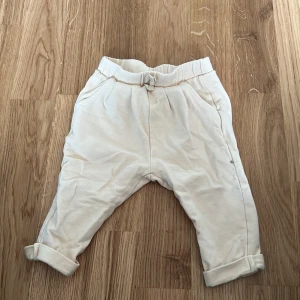 Beige byxor från Zara BabyGirl - Säljer ett par söta beige byxor från Zara BabyGirl. Byxorna har en elastisk midja och är uppvikta vid bensluten för en extra gullig look. Perfekta för de minsta att ha på sig under lek och bus.