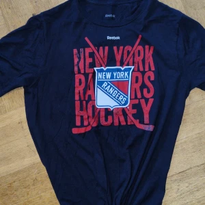 Vintage Mörkblå New York Rangers t-shirt från Reebok - Vintage Reebok med New York Rangers tryck i rött och vitt. Perfekt för 90's freaks och hockeyfans! 