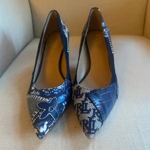 Klackskor från Ralph Lauren - Supersnygga och unika spetsklackar från Ralph Lauren. Klackarna har både läder, logo tyg, och jeans material i vitt och blått med blommiga detaljer. Gör verkligen ens outfit super cool och speciell! Helt nya och köpta för 2000kr och går inte att hitta i Sverige, men pris kan diskuteras!