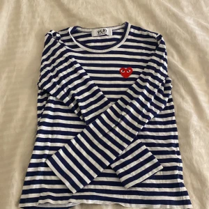 Randig långärmad tröja från Comme des Garçons - Säljer en superfin randig tröja från Comme des Garçons med det ikoniska röda hjärtat på bröstet. Tröjan är blå och vit med långa ärmar, perfekt för både vår och höst. Den är i mycket bra skick och passar till alla tillfällen. Den är i storlek L men passar mig som S då den blir kort vid armarna. 