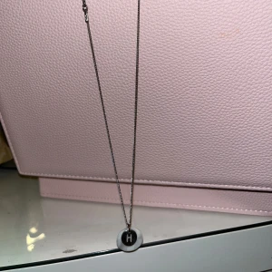 Silverfärgat halsband med bokstavsberlock - Elegant silverfärgat halsband med en rund berlock som har bokstaven 'H'. Perfekt för att ge en personlig touch till din stil.