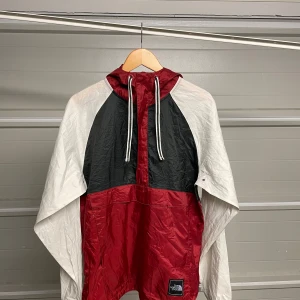 Röd och svart vindjacka från The North Face - Säljer en snygg röd och svart vindjacka från The North Face. Jackan har en praktisk huva med dragsko och långa ärmar. Perfekt för blåsiga dagar och har en cool färgblockdesign. Passar både till vardags och utomhusaktiviteter. Säljes i befintligt skick. Storlek: M