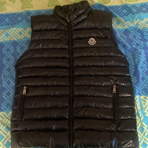 Svart Moncler Väst - Svart väst från Moncler med dragkedja hela vägen upp. Använd i ett par månader men säljer pga jag har köpt en ny i blå. 