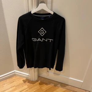 Svart långärmad tröja från GANT - Snygg svart långärmad tröja från GANT med en vit loga på framsidan. Hör av dig vid frågor eller funderingar.
