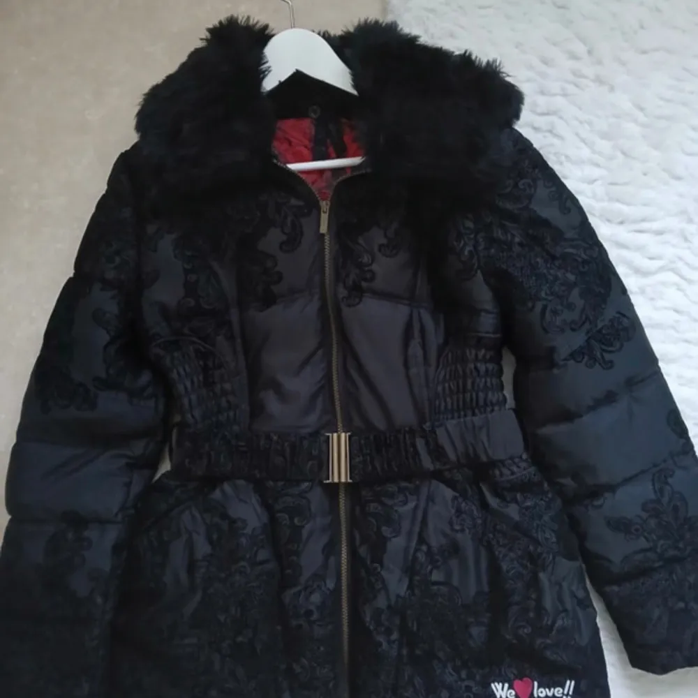 Snygg svart vinterjacka från Desigual med faux fur och broderade mönster. Jackan har en dragkedja framtill och ett elastiskt bälte i midjan. Insidan är fodrad med ett rött mönster. I princip oanvänd. Nypris ca 2000kr OBS! Liten i strl! Är snarare strl 42. Jackor.