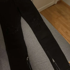 Svarta jeans med dragkedja - Säljer ett par svarta jeans i bra skick. De har en tight passform med snygga slitningar på knäna och dragkedjor vid anklarna. Perfekta för en cool och avslappnad stil. Passar både till vardags och fest!