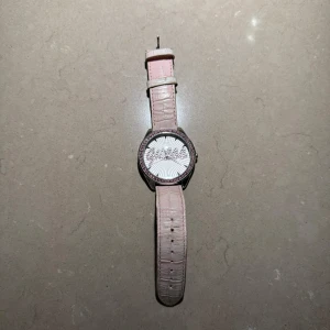 Rosa klocka från Guess - Säljer en snygg rosa klocka från Guess med ett glittrigt urverk och rosa stenar runt boetten. Armbandet är i skinn med krokodilmönster. Perfekt för att ge lite bling till din outfit! 🕒✨