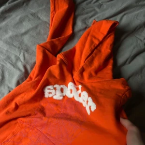 Orange hoodie från Sp5der - Säljer en orange hoodie från Sp5der med vit broderad text på framsidan. Perfekt för en avslappnad stil. Använd kanske 5 gånger. jag tröttnade på den ljusa orange färgen. Size M
