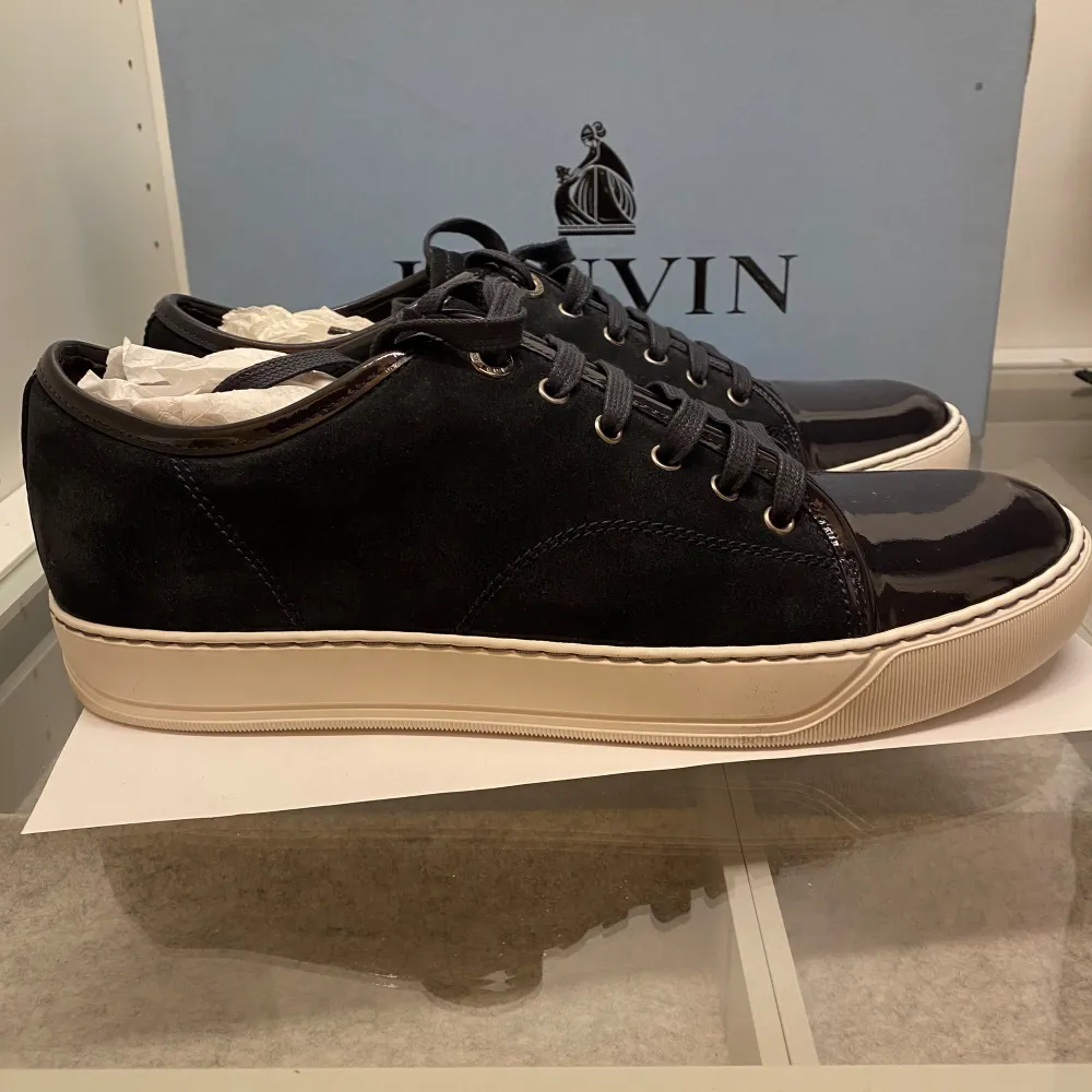 Säljer ett par stilrena mörkblåa sneakers från Lanvin i mycket bra skick. Skorna har en snygg kombination av skinn och syntet med en glansig tå och klassisk snörning. Perfekta för både vardag och fest! Storlek 9UK (allt og medföljer). Skor.