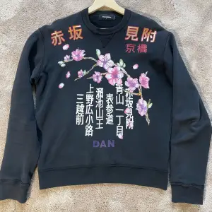 Säljer en svart sweatshirt från dsquared med ett snyggt blommigt tryck.. Tröjan har långa ärmar och en bekväm passform. Perfekt för både vardag och avslappnade tillfällen. Text i rött och vitt ger en unik touch. Passar bra till jeans. Storlek L, passar även M. 