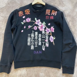 Dsquared sweatshirt med blommigt tryck - Säljer en svart sweatshirt från dsquared med ett snyggt blommigt tryck.. Tröjan har långa ärmar och en bekväm passform. Perfekt för både vardag och avslappnade tillfällen. Text i rött och vitt ger en unik touch. Passar bra till jeans. Storlek L, passar även M. 