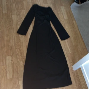 Svart långklänning med snörning - Säljer en elegant svart långklänning med snörning i midjan. Klänningen har långa ärmar och är perfekt för festliga tillfällen. Den är i nyskick och har en tight passform som framhäver figuren. Materialet känns mjukt och bekvämt mot huden.