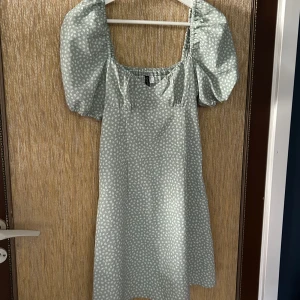 Ljusgrön blommig klänning från HM - Säljer en superfin ljusgrön klänning från HM med små vita blommor. Klänningen har puffiga kortärmar och en söt fyrkantig urringning. Perfekt för sommarens alla fester och midsommarfiranden! 🌸Är i bra skick