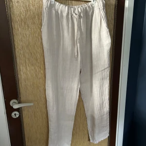Beige linnebyxor med snörning - Säljer ett par superbekväma beige linnebyxor. De har en avslappnad passform med snörning i midjan för justerbarhet. Perfekta för varma sommardagar eller en avslappnad dag hemma. Byxorna har också praktiska fickor på sidorna. Köpta på en marknad så finns inget specifikt märke på dom.