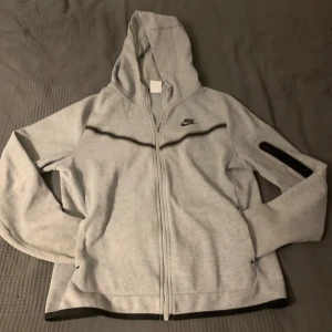 Oanvänd Grå Nike Tech Fleece Hoodie Storlek 158-170 cm - Modern och Stilren Design för Optimal Komfort och Värme, Perfekt för Höst- och Vinterdagar, Högkvalitativ - Säljer en grå Nike Tech Fleece i storlek 158-170 cm, helt oanvänd. Den är för liten för mig, så jag behöver tyvärr sälja den vidare. Perfekt för höst- och vinterbruk.