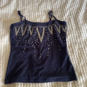 Mörkblå linne från Gianini - Säljer ett snyggt mörkblått linne från Gianini. Det har tunna axelband och är dekorerat med glittriga paljetter i ett coolt mönster framtill. Perfekt för en festlig kväll eller när du vill glittra lite extra!