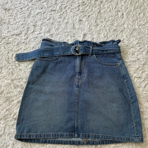 Jeanskjol från H&M Divided - Säljer en snygg jeanskjol från H&M Divided i storlek 38. Kjolen är i en klassisk blå jeansfärg och har en medföljande bälte som ger en extra touch. Den har två fickor bak och en bekväm passform. Perfekt för både vardag och fest!💗