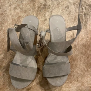 Grå kilklackssandaler från New Look - Säljer ett par snygga grå sandaler med kilklack från New Look. De har en bekväm passform med breda remmar i mocka och en cool korkklack. Perfekta för sommaren och passar både till vardags och fest!